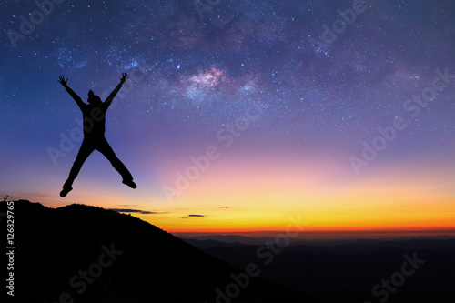 Silhouette of woman is jumping on top of mountain and enjoy to see the milky way before sunrise.