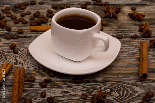 Small white cup of coffee, cinnamon sticks, cocoa beans, star anise on wooden background