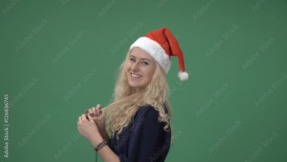 Young blonde woman in a red christmas cap smiling and playing with hair, chroma key green screen Young blonde woman in a red christmas cap smiling and playing with hair, chroma key green screen