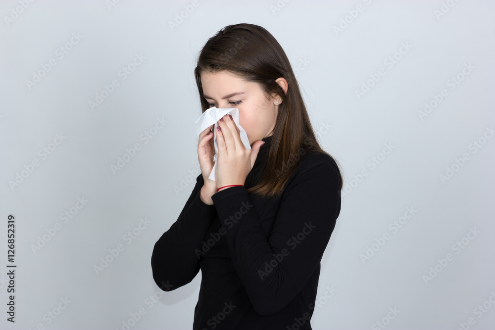 Portrait of a pretty woman in turtleneck sweaterand having flu. girl blowing nose standing over gray background Portrait of a pretty woman in turtleneck sweaterand having flu. girl blowing nose standing over gray background