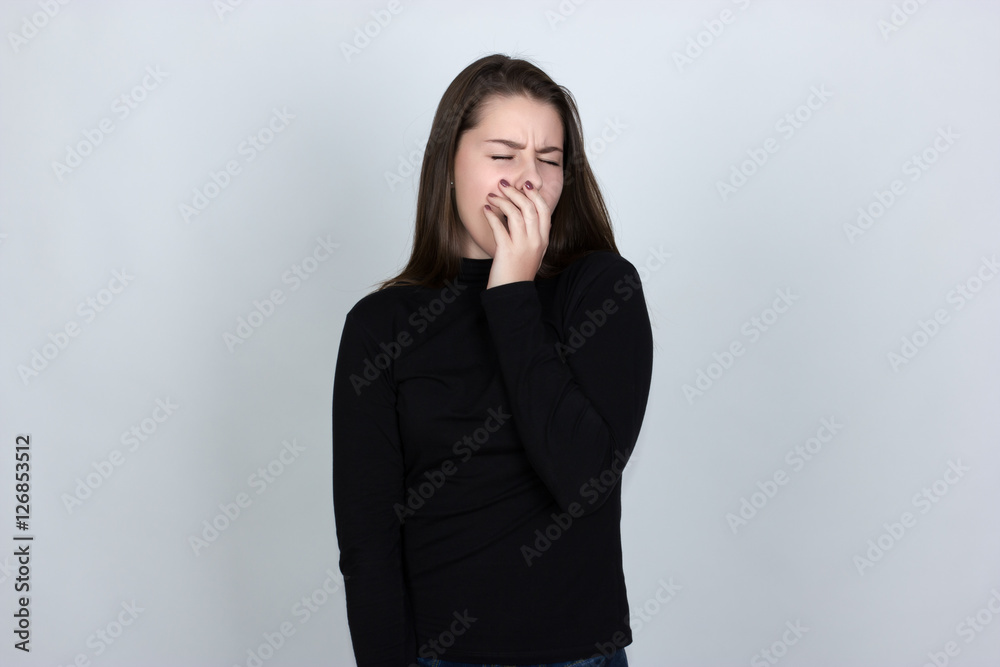 Portrait of a pretty woman in turtleneck sweater yawns she covers her mouth standing over gray background Portrait of a pretty woman in turtleneck sweater yawns she covers her mouth standing over gray background