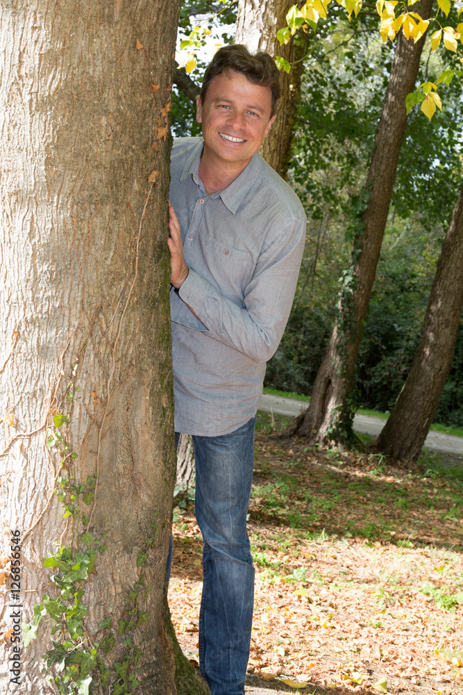 Charming man in blue shirt leaning on tree in park Charming man in blue shirt leaning on tree in park