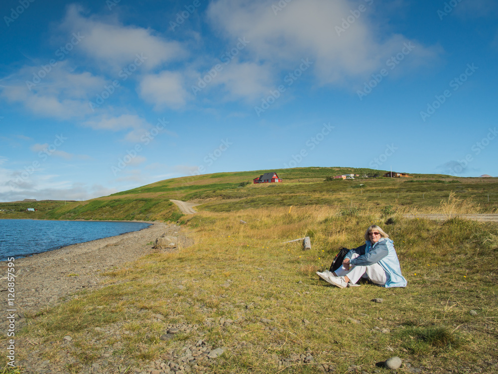 Senior woman is sitting on the grass at Vatnsnes, Iceland