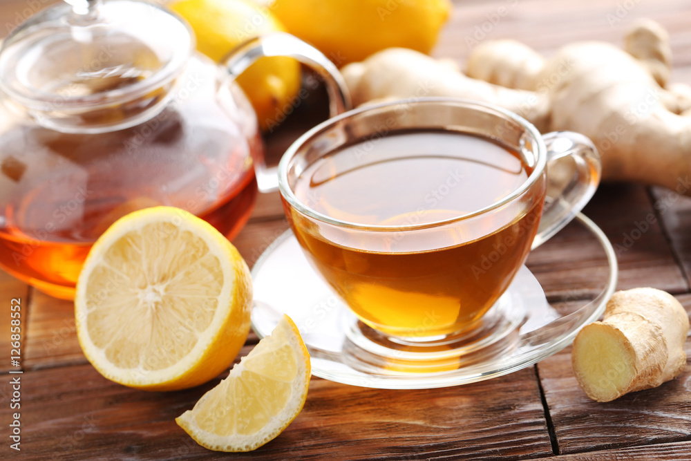 Cup of tea with ginger root and lemon on brown wooden table