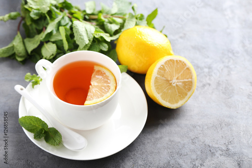 Cup of tea with mint and lemon on grey wooden table