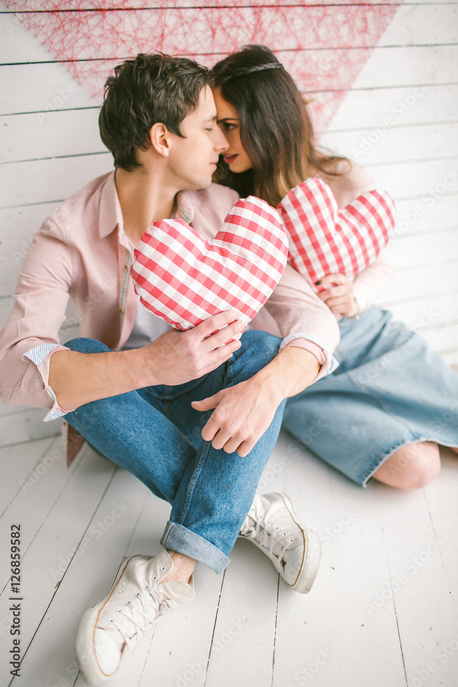 Fototapeta premium Young couple with heart-shaped pillows posing for love-story in