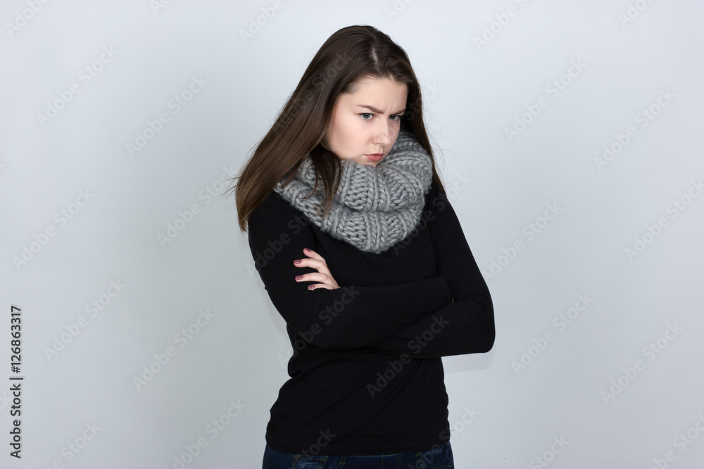 Portrait of a pretty offended sad gir in turtleneck sweater with scarf over gray background Portrait of a pretty offended sad gir in turtleneck sweater with scarf over gray background