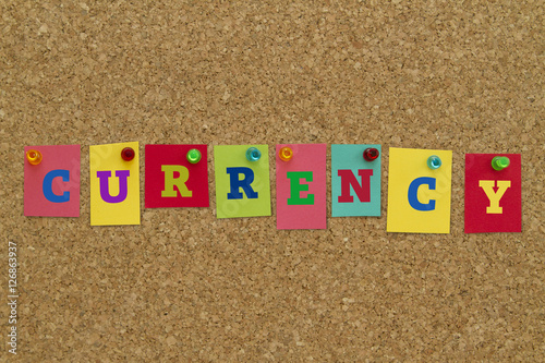 Currency word written on colorful sticky notes pinned on cork board.