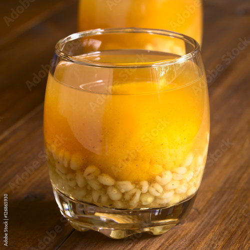 Traditional Chilean summer drink Mote con Huesillo, made of dried peaches and cooked husked wheat, photographed with natural light (Selective Focus, Focus on the front of the drink) photo