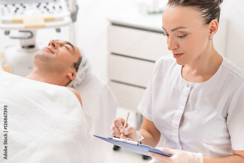 Fototapeta premium Professional cosmetologist making notes before procedure