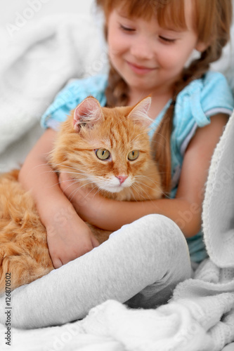 Cute little girl and red cat on sofa, closeup