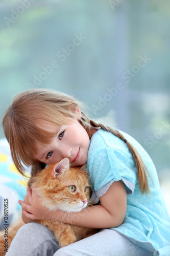 Cute little girl with red cat on window background