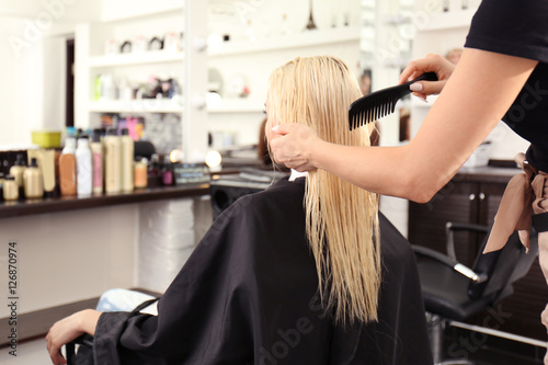 Hairdresser combing blonde's hair at salon