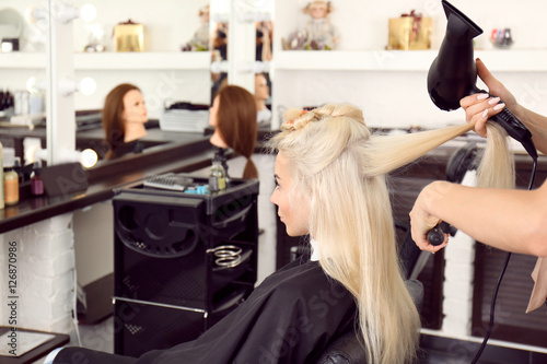 Hairdresser drying blonde s hair at salon