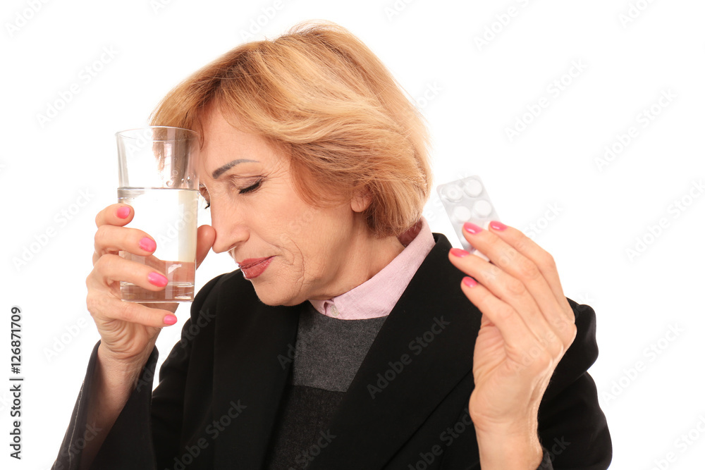 Portrait of senior woman suffering from headache and holding glass of water and medicines, isolated on white