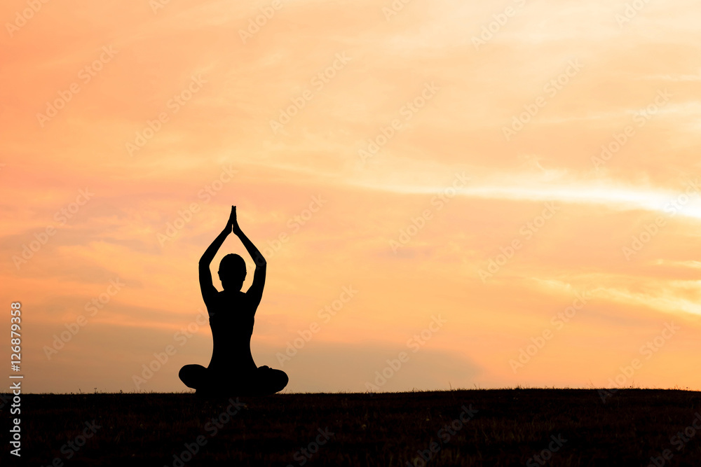 Silhouette of woman practicing yoga at sunset