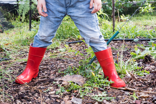 Cropped view of child in red gumboots and denim jeans in garden (selective focus)