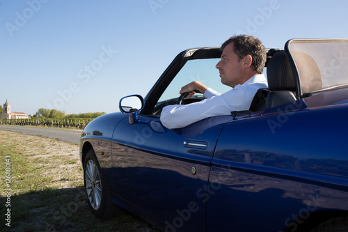 Happy man in a blue convertible car smiling