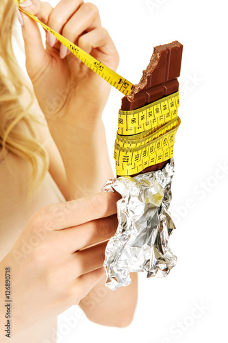 Young woman holding chocolate and eating measure tape photo