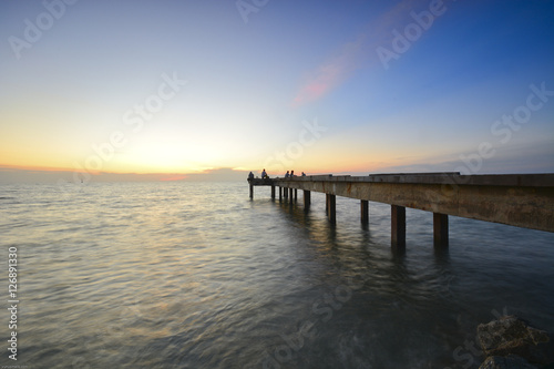 Beautiful dusk sky over the long jetty with silhouette of anglers. Long exposure shot of seascape.