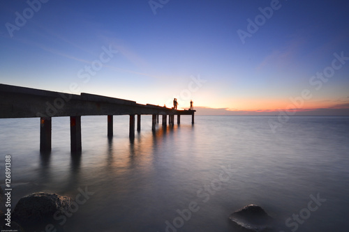 Beautiful dusk sky over the long jetty with silhouette of anglers. Long exposure shot of seascape.
