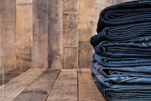 Stack of blue jeans on old wood background