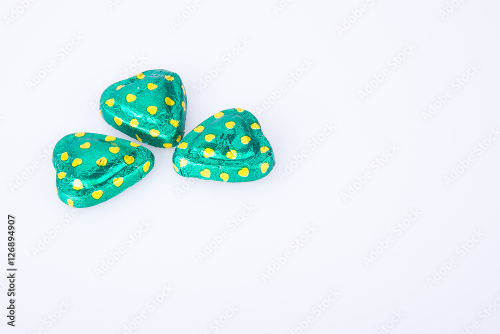 Chocolate or green foil heart-shaped chocolate on a background. Chocolate or green foil heart-shaped chocolate on a background.