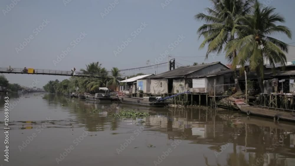BOAT POV WS PAN Riverbank with Footbridge and Houses / Vietnam BOAT POV WS PAN Riverbank with Footbridge and Houses / Vietnam
