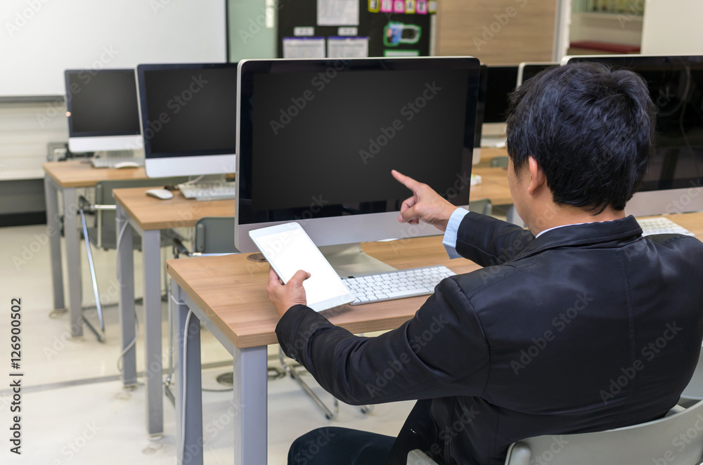 Rear view of a businessman working with a computer and tablet at Rear view of a businessman working with a computer and tablet at