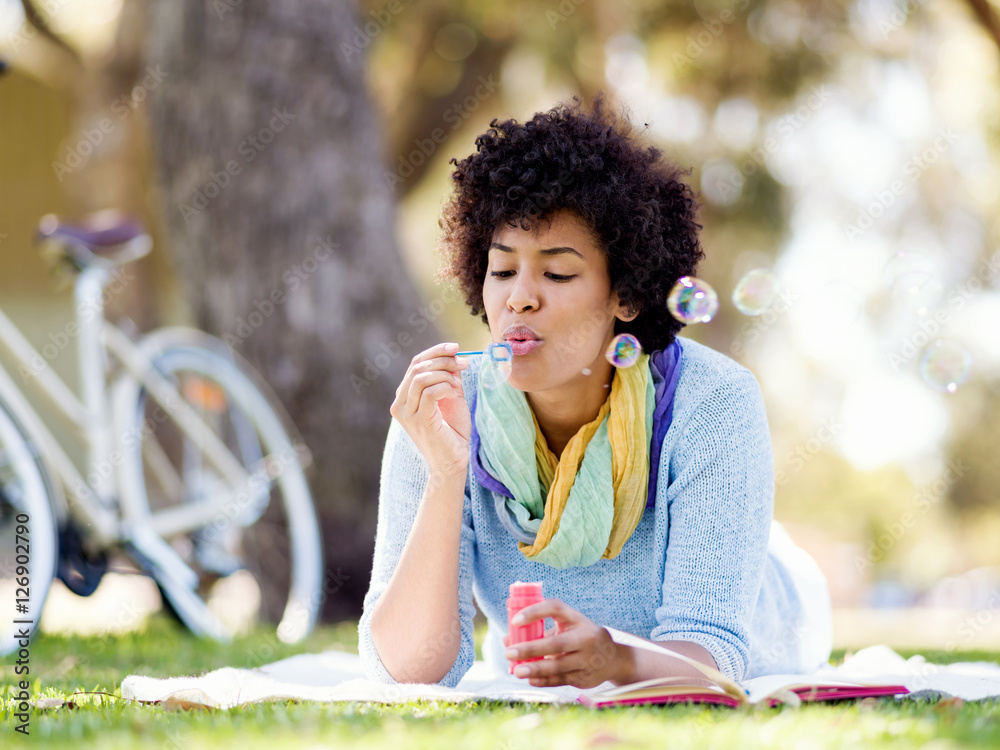 Fototapeta premium Beautiful woman blowing bubbles in park
