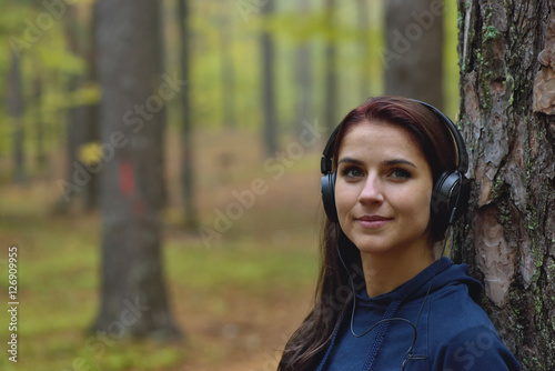 Beautiful and happy girl listens to music in headphones in nature. Autumn forrest in the background