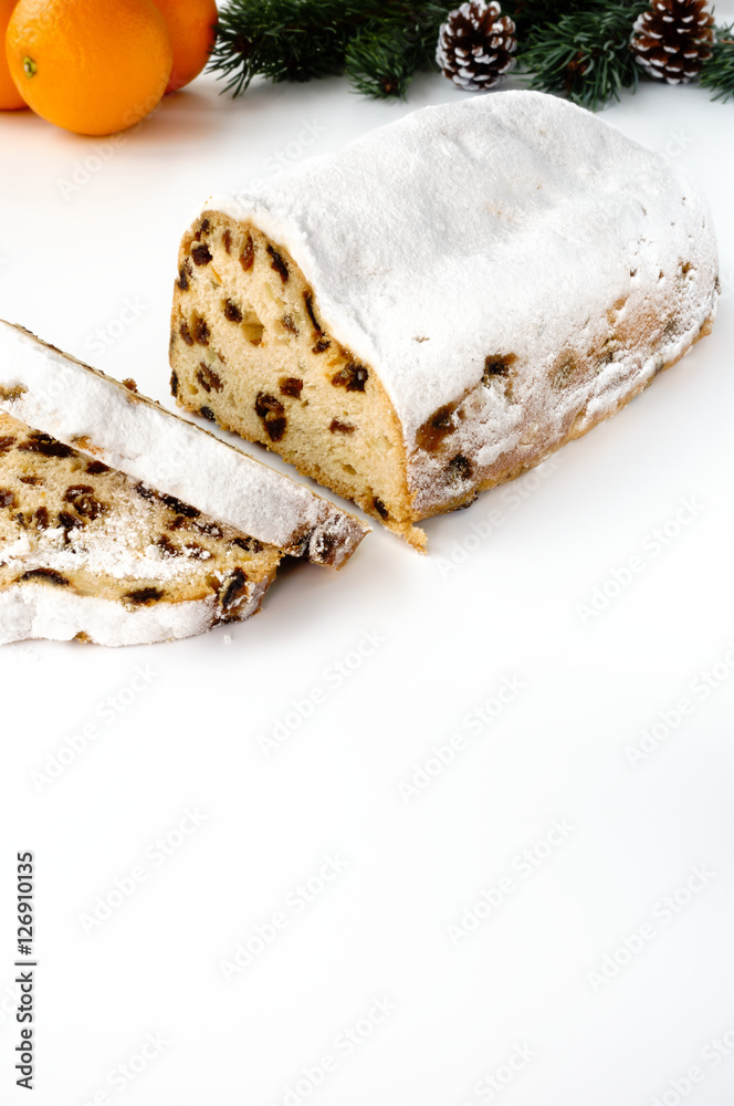 Sliced Christstollen on white background with fresh oranges, fir and pine cones in the background. In the foreground lots of copy space.