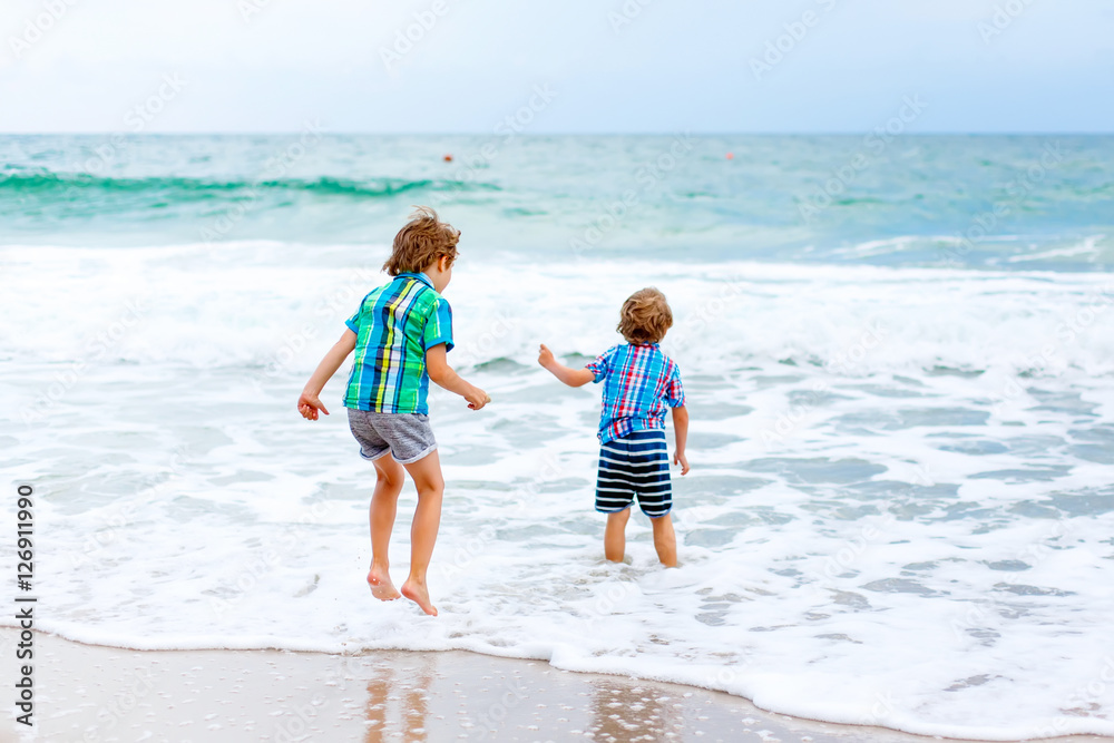 Two little kids boys running on the beach of ocean Two little kids boys running on the beach of ocean