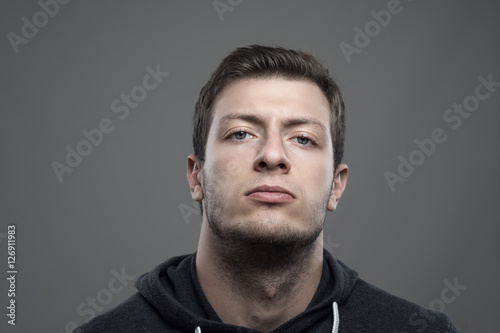 Moody portrait of proud young man with head leaned back looking at camera over gray background