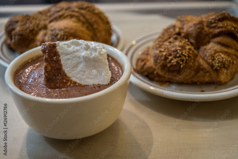 Hot chocolate with marshmallow and croissants in the background