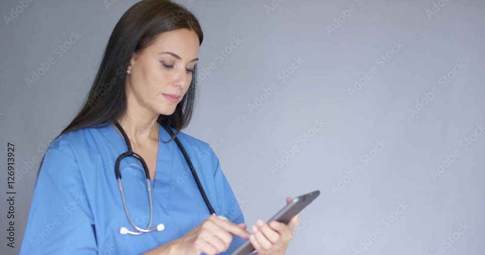 Thoughtful young woman doctor in surgical scrubs standing holding a tablet as she looks into the air with a contemplative expression with copy space Thoughtful young woman doctor in surgical scrubs standing holding a tablet as she looks into the air with a contemplative expression with copy space