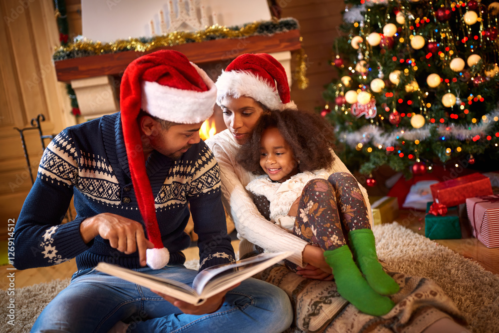 young dad reading a book to cute daughter near Christmas tree young dad reading a book to cute daughter near Christmas tree