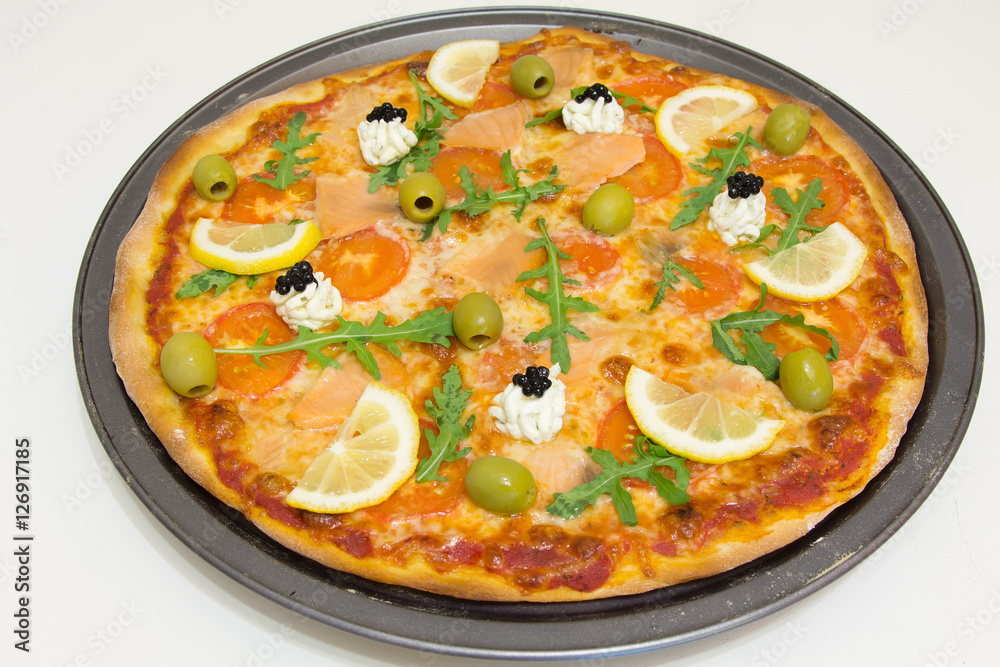 Pizza with salmon, olives, arugula and lemon on a white wooden table, selective focus