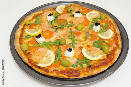Pizza with salmon, olives, arugula and lemon on a white wooden table, selective focus