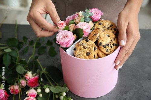 Female florist preparing box with beautiful flowers and cookies, closeup