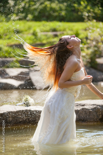 Junge schöne Frau mit weißen Brautkleid schwingt ihre Haare in Fächerform als sie mit dem Kopf aus dem Wasser kommt. photo