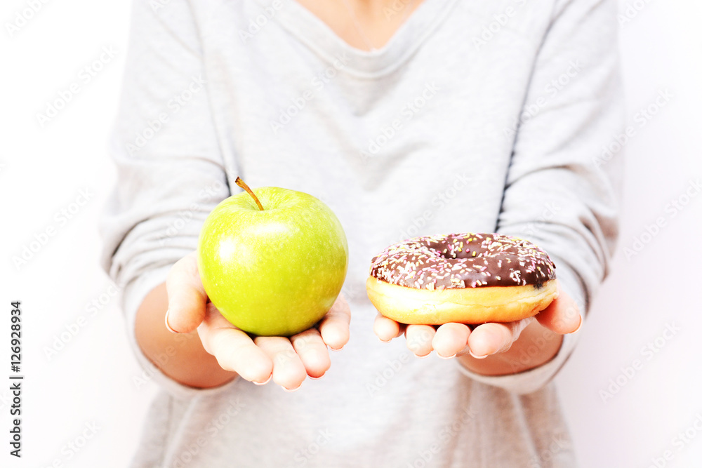 Dieting concept with young woman choosing between healthy fruits and sweets, holding green apple and tasty chocolate donut Dieting concept with young woman choosing between healthy fruits and sweets, holding green apple and tasty chocolate donut
