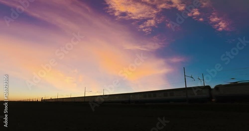 Silhouette of an Italian Intercity Passenger Train is Passing in front of a beautiful pink sky at the Sunset. photo