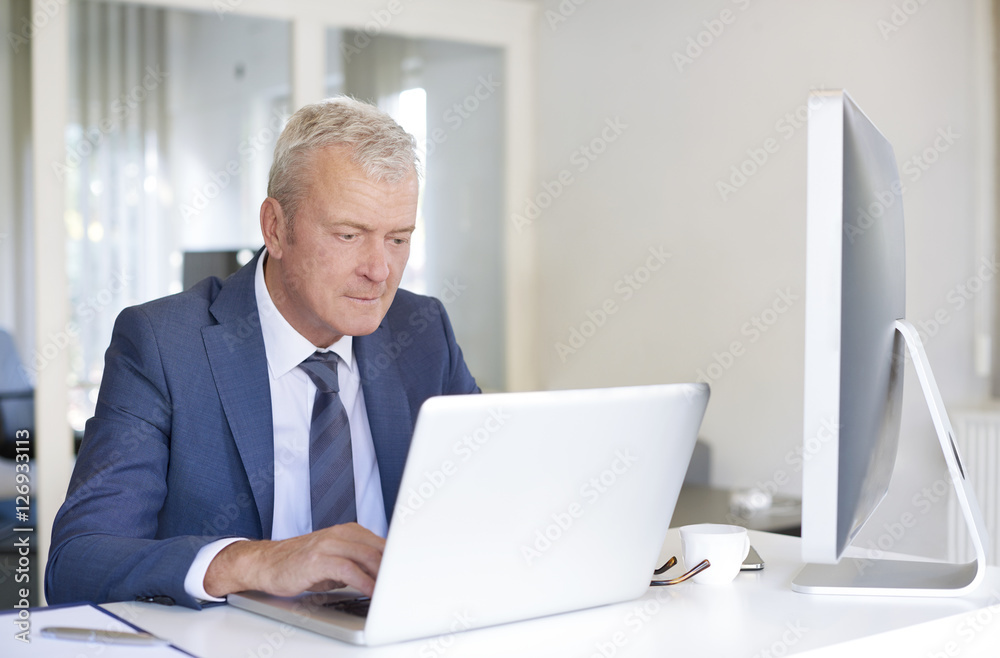 Close-up shot of an executive senior sales man sitting at office and working on his laptop.