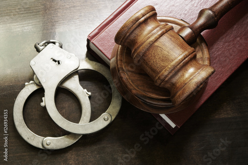 Gavel and handcuffs with red legal book on wooden table