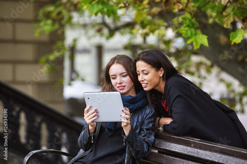 two beautiful young girls , look at the photos on your tablet , socializing on the Internet