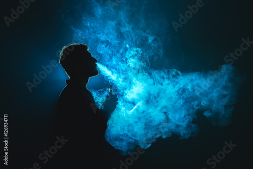 The man smoke a cigarette against the background of the blue light