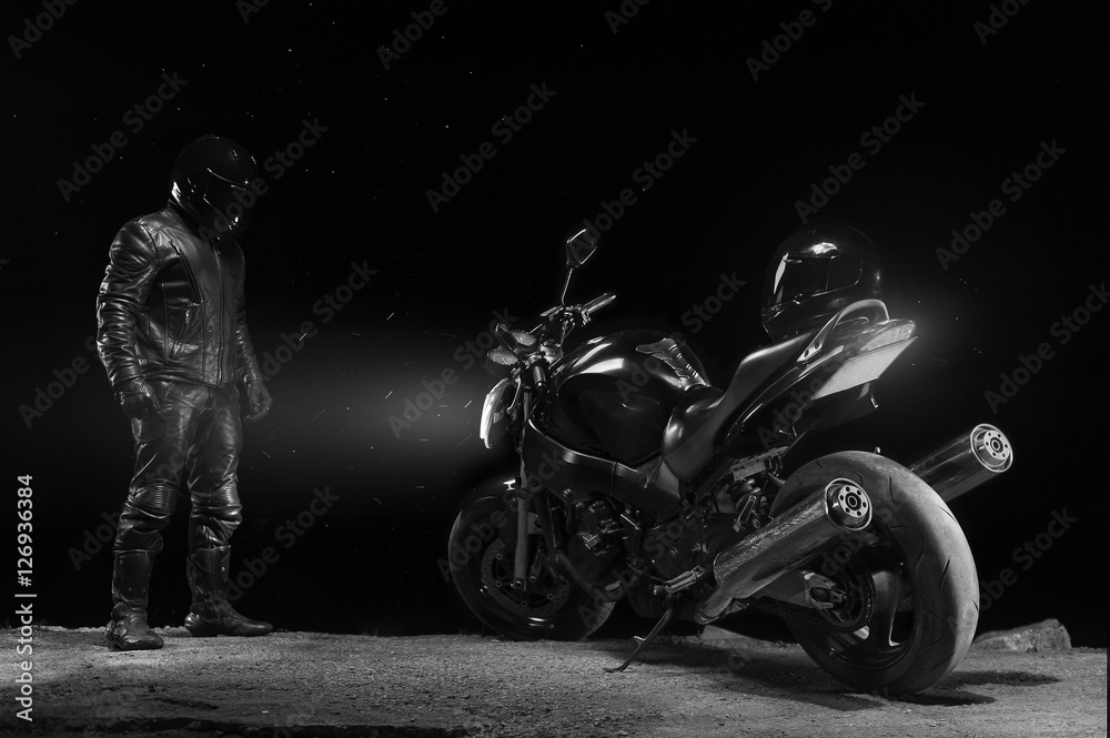 Fototapeta premium Male biker in leather outfit standing next to bike