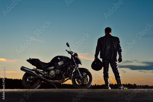 Male biker in leather outfit standing next to bike