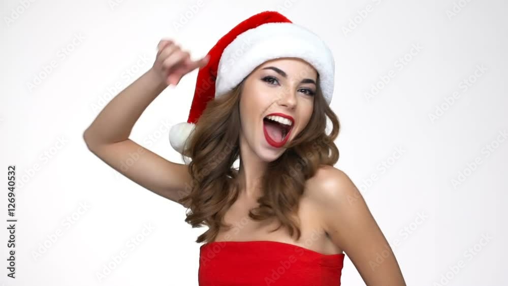 Happy cheerful girl in red santa claus costume looking sideways and pointing finger at camera Happy cheerful girl in red santa claus costume looking sideways and pointing finger at camera